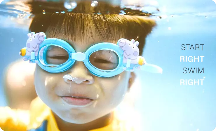 Child wearing the Peppa Pig George blue goggles and submerging his head in the water at the shallow swimming pool for beginners swimming class with 'start right,swim right' poster